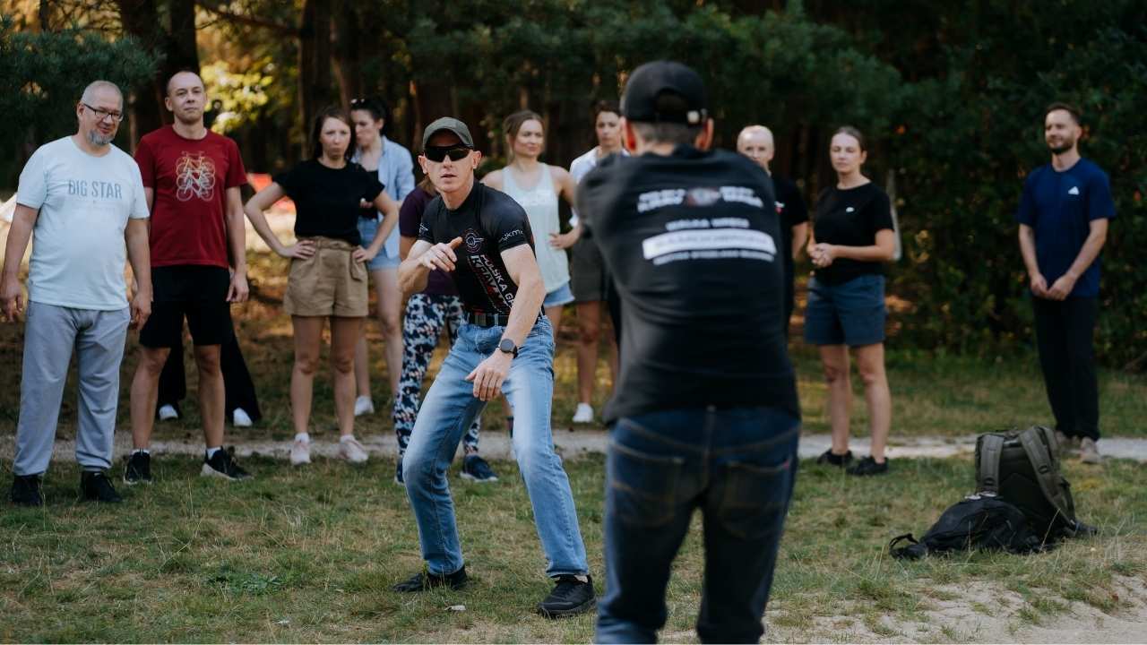 instruktorzy pokazują techniki samoobrony i ludzie obserwujący pokaz w lesie